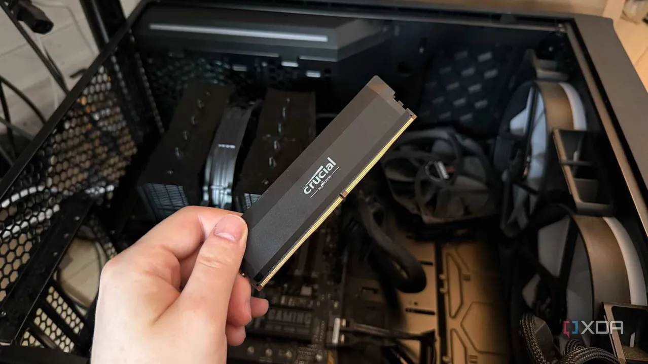 A photo of someone holding a RAM stick in front of a PC with the side panel off